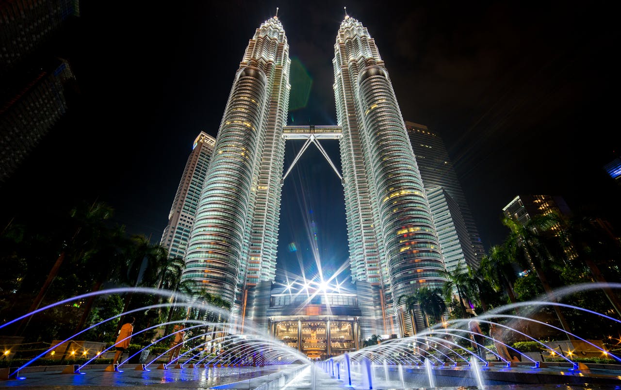 why-choose-us-01 Stunning night view of the illuminated Petronas Twin Towers in Kuala Lumpur with fountains in the foreground.